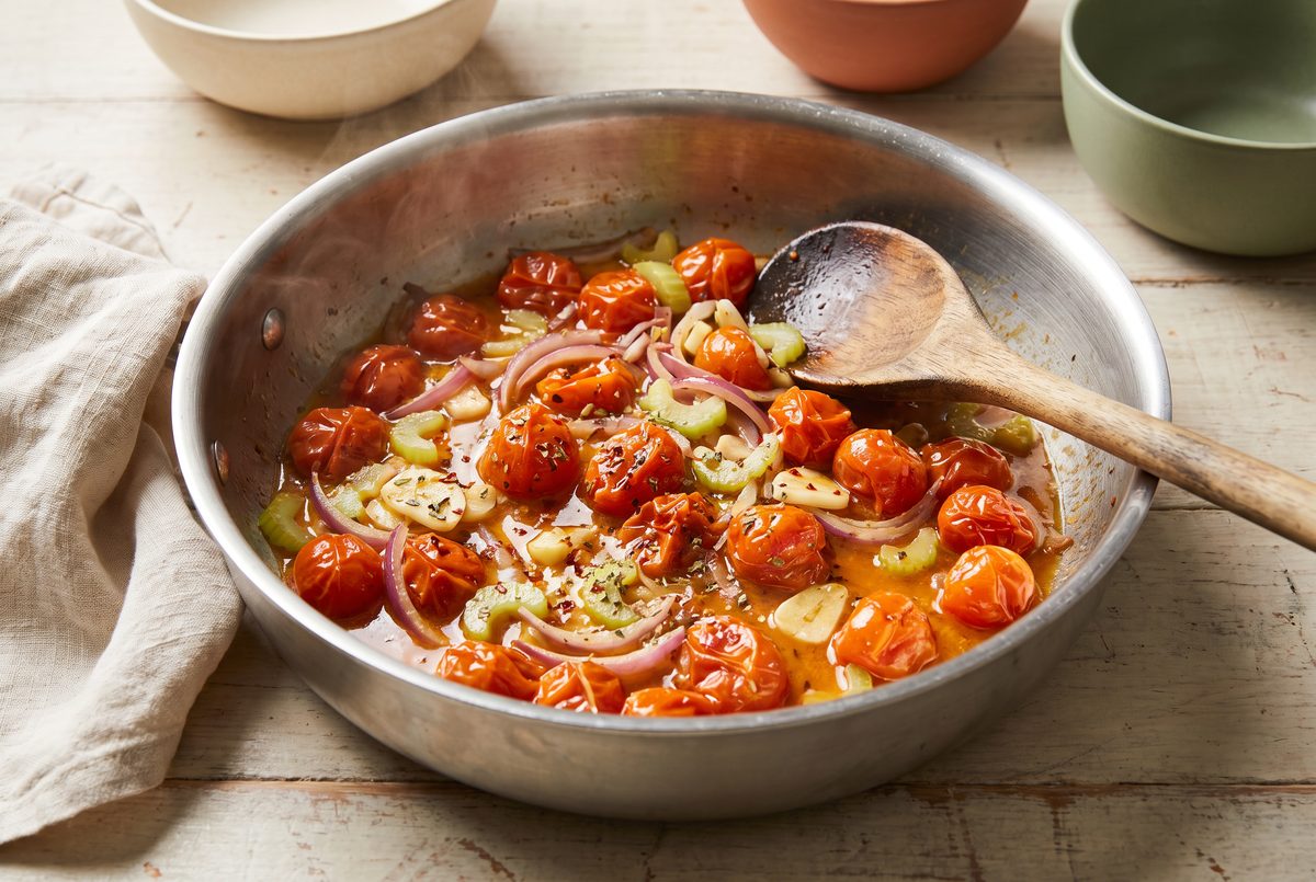 Halved cherry tomatoes collapsed into a glossy sauce with sliced onion and celery in a skillet