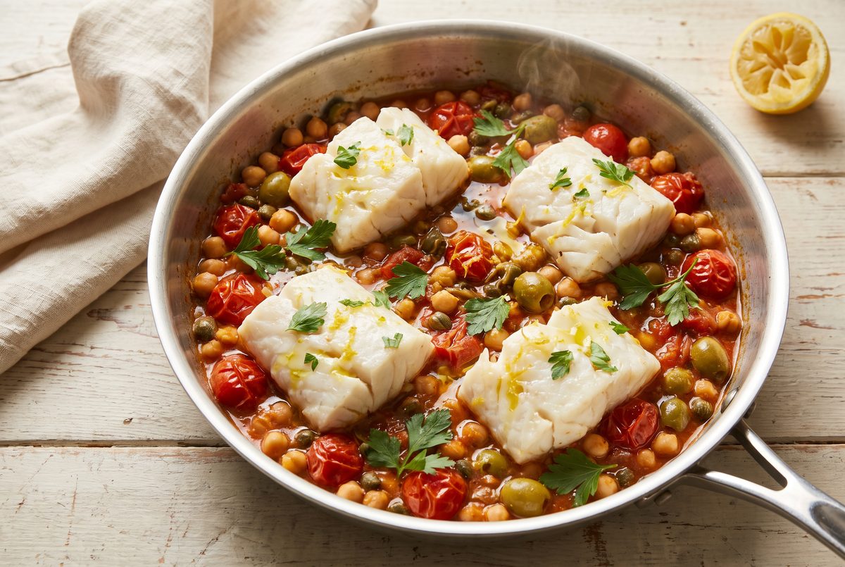 The finished pan of baked cod on chickpeas and tomatoes, strewn with parsley and lemon zest