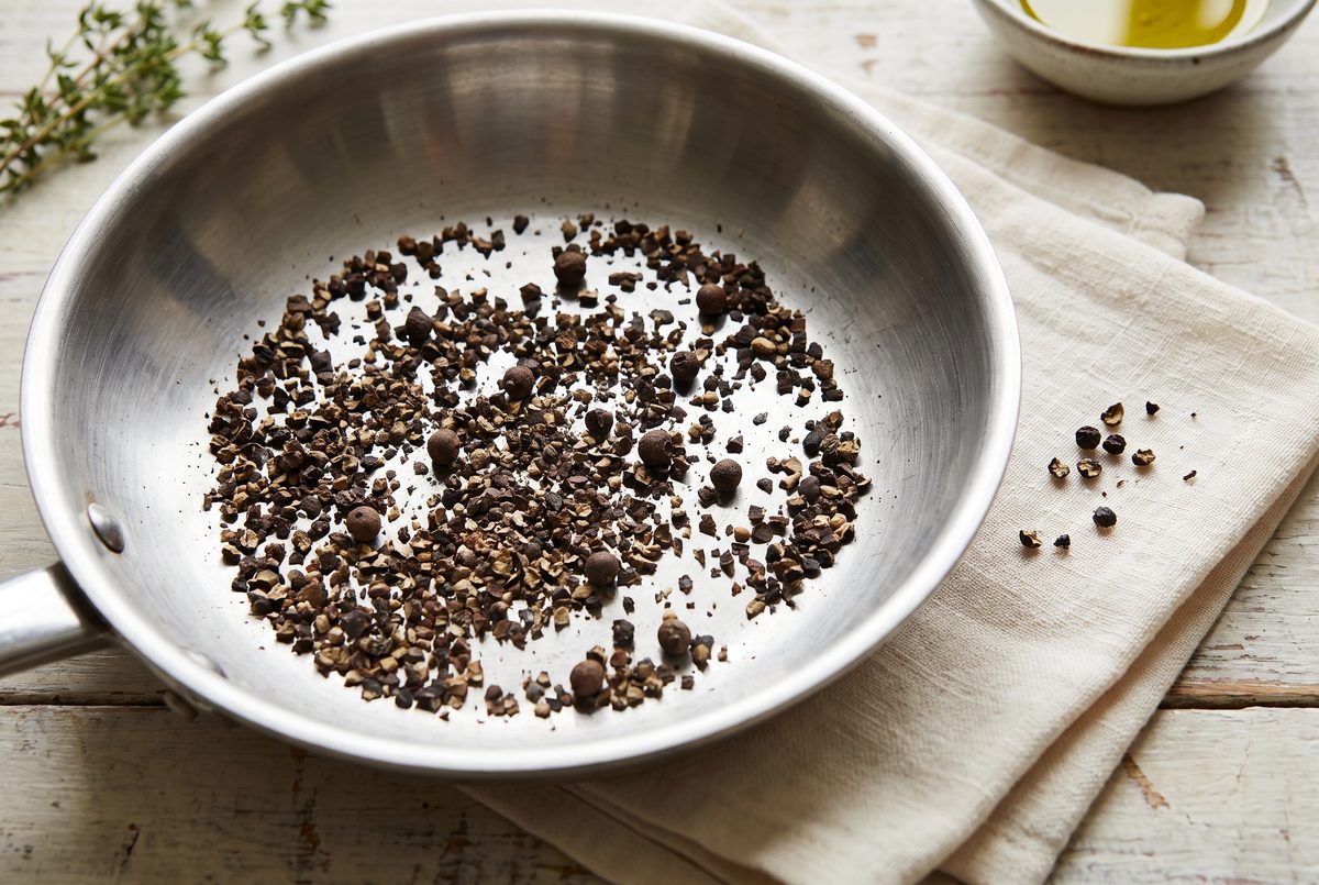 Coarsely cracked black peppercorns, some pieces still nearly whole, in a dry stainless-steel pan