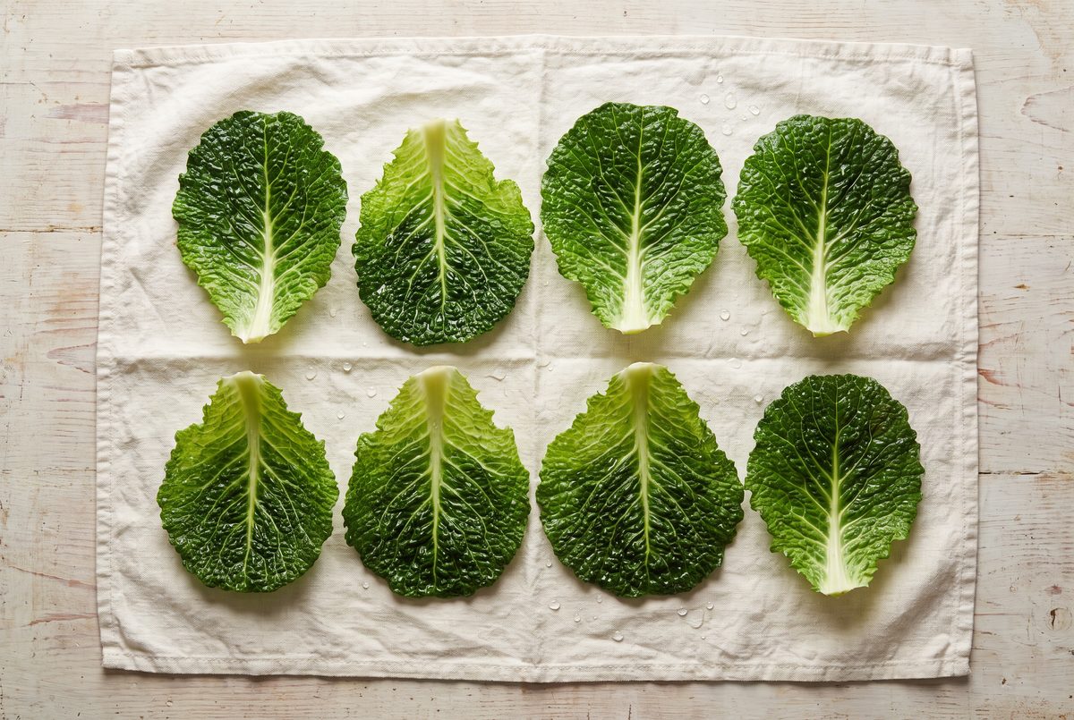 Savoy cabbage leaves laid out flat on a cream linen towel, each with its broad pale central rib