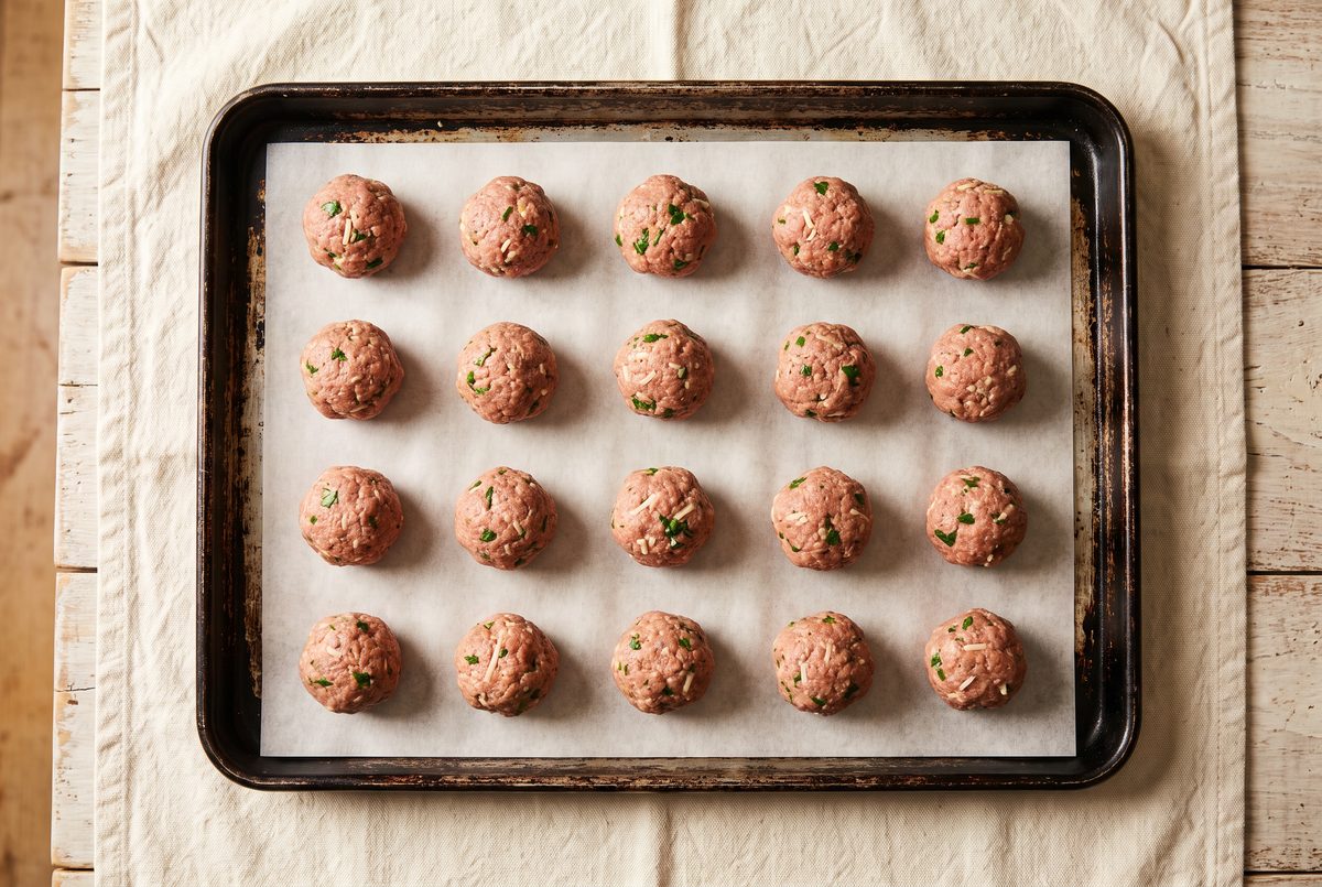 Twenty raw meatballs spaced evenly on a parchment-lined sheet pan