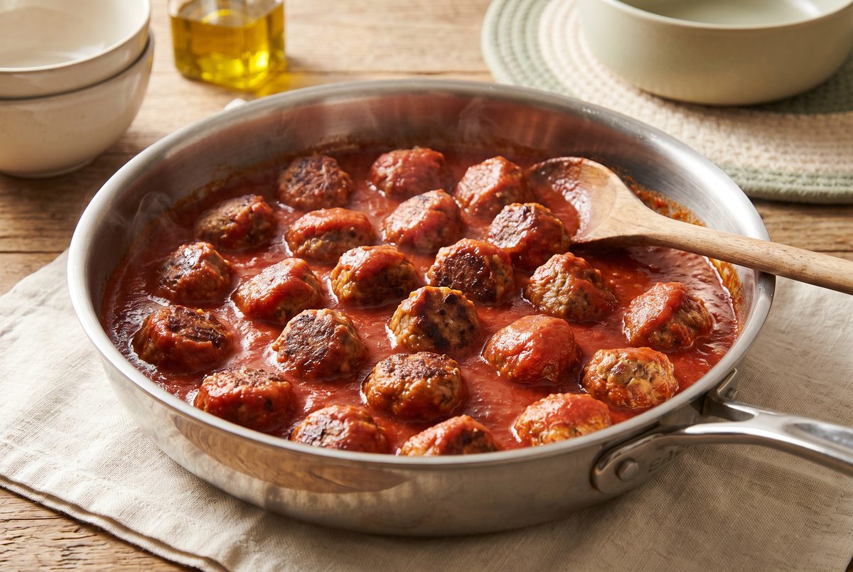 Meatballs half-submerged in tomato sauce in a wide shallow pan