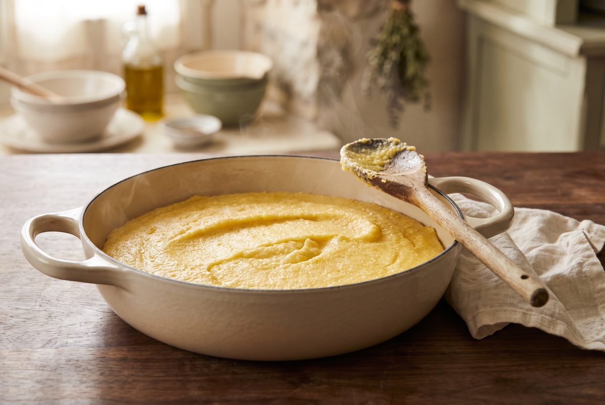 Soft golden polenta in a heavy pot, thick enough to hold a channel left by a wooden spoon, the spoon resting against the rim