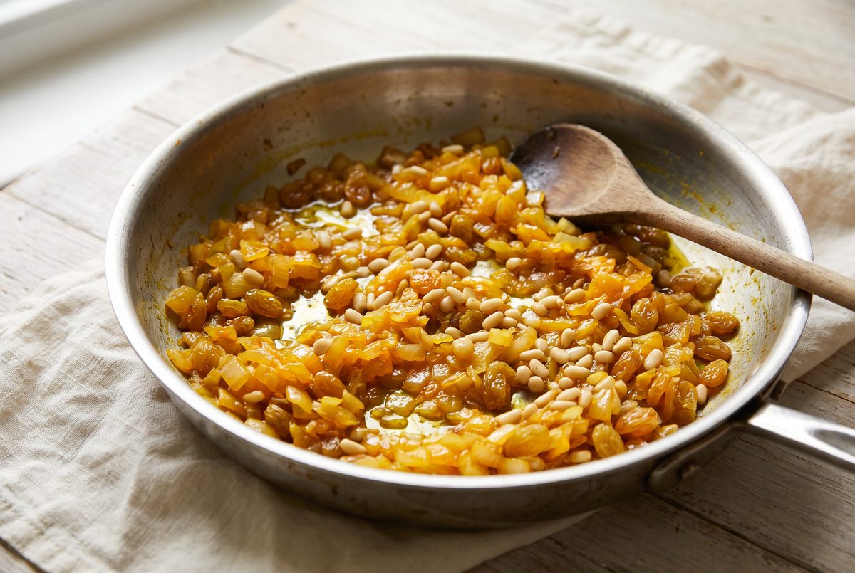 Softened onion, raisins and pine nuts in a deep orange-gold saffron base in a wide stainless-steel skillet