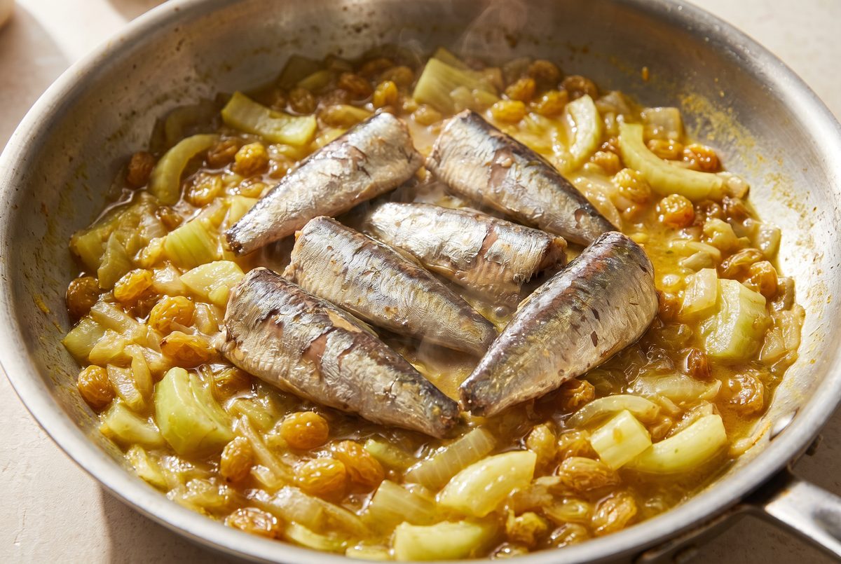 Large pieces of sardine fillet resting in a saffron-gold fennel sauce in a stainless-steel skillet