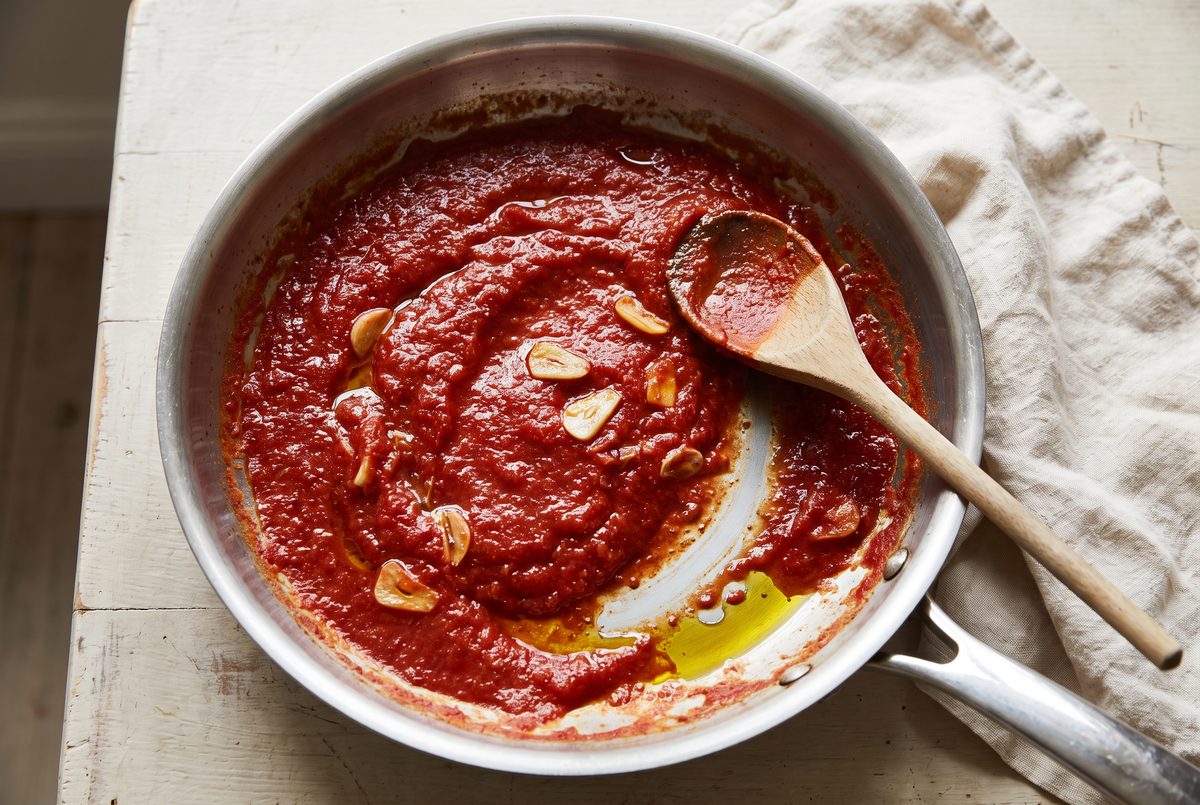 Tomato sauce thickened in a wide pan, a wooden spoon resting against the rim