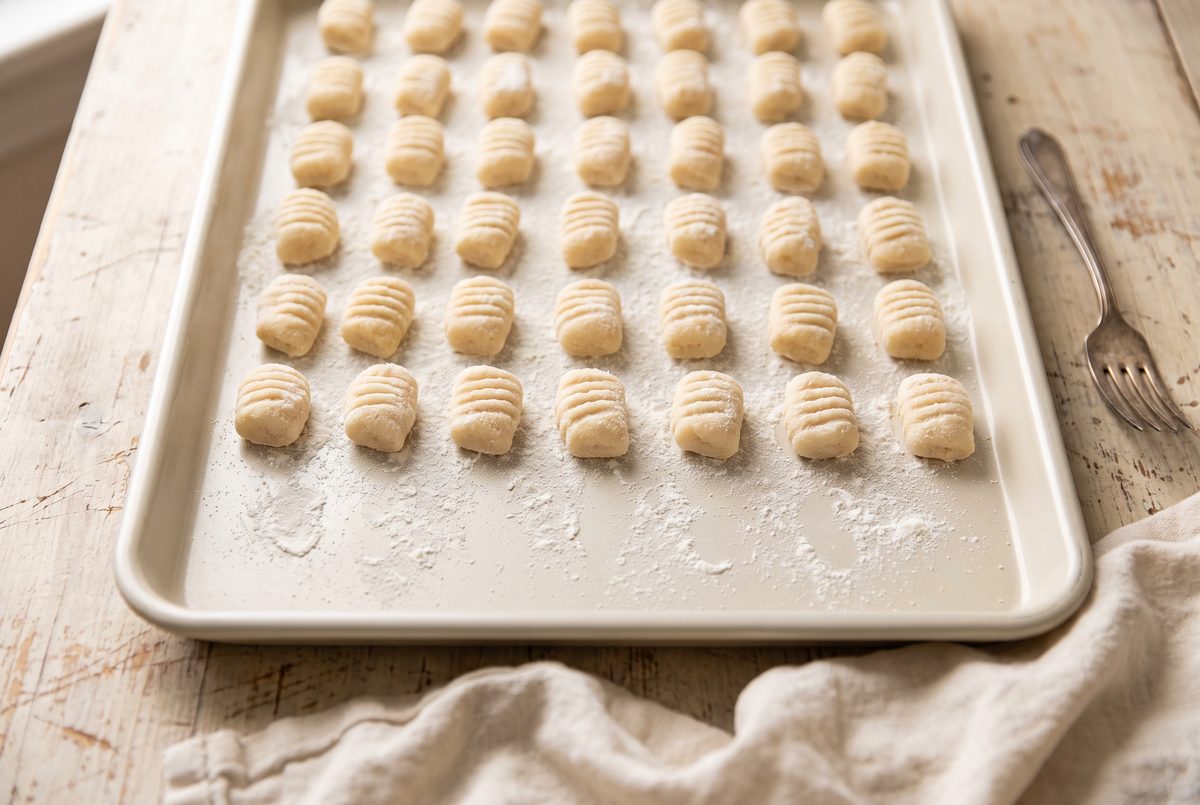 Rows of ridged raw gnocchi on a floured sheet pan