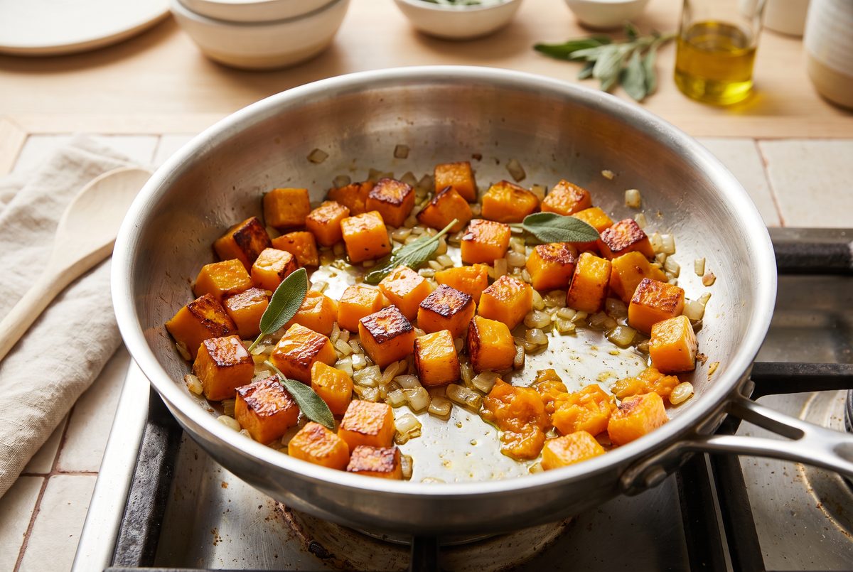 Cubes of butternut squash and diced onion with caramelized golden edges in a wide pan