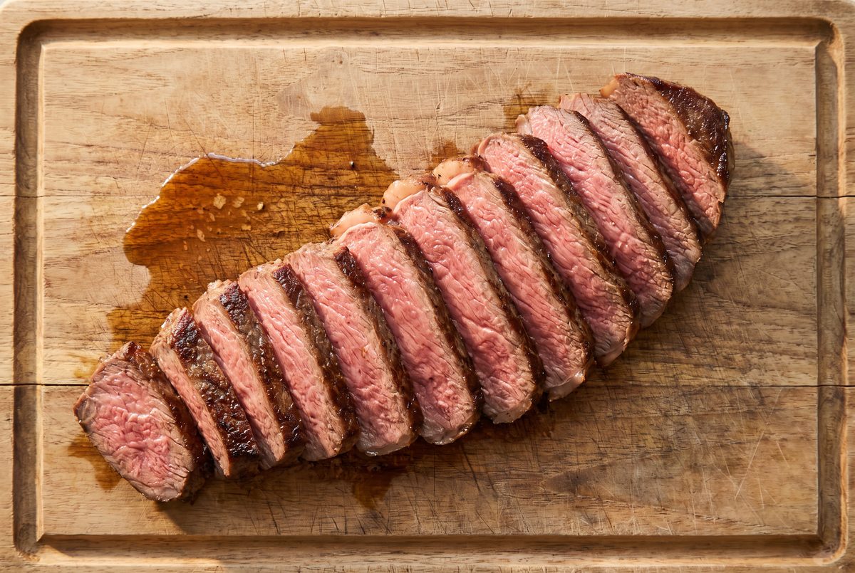 Sliced sirloin steak fanned out on a wooden board, each slice rosy pink in the middle with a dark seared edge, juices pooling on the board
